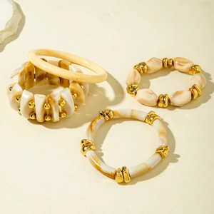 Close-up of irregular marbled acrylic beaded bracelets with gold accents on stone base