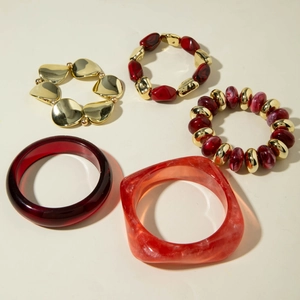 Detail of red resin bangles and gold CCB tube stretch bracelets with leaf charm