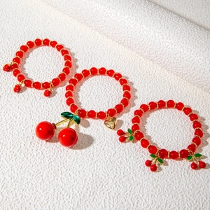 Three-piece red cherry beaded bracelet set with golden heart charms on white background