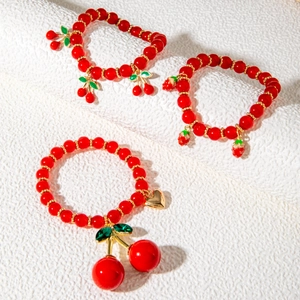 Detail of red cherry and strawberry beaded bracelets with gold accents and heart charms