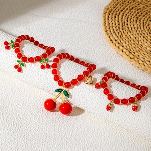 Detailed view of red cherry and strawberry beaded bracelets with gold heart charms