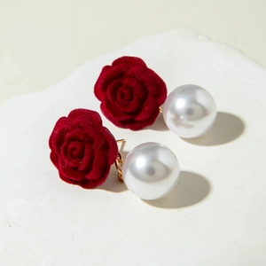 Detailed view of red velvet rose earrings with large white pearls on a stone base