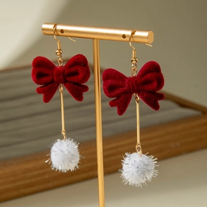 Red velvet bow earrings with festive white tinsel pom-poms on a gold jewelry stand