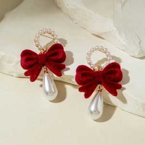 Detail of red velvet bow earrings with teardrop pearls on a textured stone surface