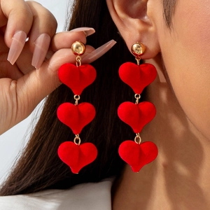 Detail of red velvet triple heart drop earrings with gold studs worn by model