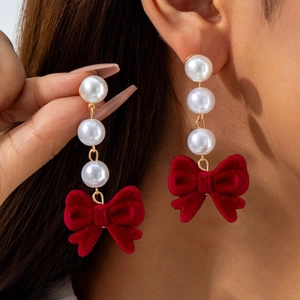 Detail view of red velvet bow earrings with three round white pearls and gold metal links