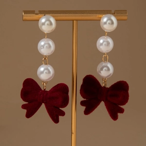 Detail of red velvet bow earrings with white imitation pearls on a golden display stand