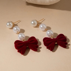 Macro view of red velvet bow and layered pearl drop earrings with elegant gold finish