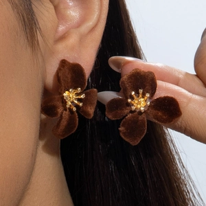 Macro view of brown velvet flower earrings with gold center worn on a model's ear