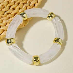 Detail of white marble acrylic tube bracelet with golden spacers on a cream background