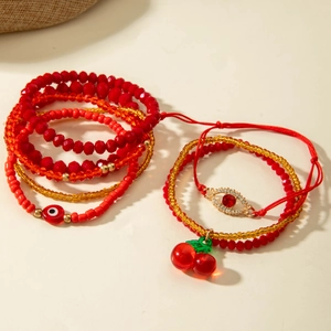 Red beaded bracelet set featuring cherry charms and evil eye details on warm background