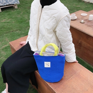 Vue détaillée du sac en toile matelassée bleue avec anses jaunes et logo de mouton