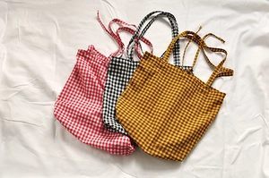 Detail von karierten Canvas-Taschen mit Bindebändern in Rot, Schwarz und Ingwergelb