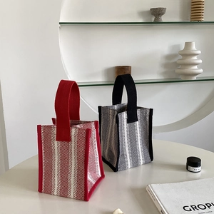 Close-up of vertical striped knitted tote bags with sturdy wide handles on a minimalist table