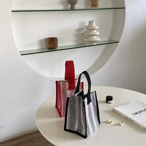 Detail of knitted canvas tote bags with red and black stripes on a stylish table