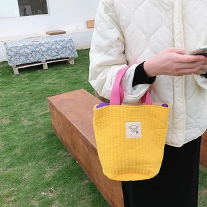 Détail d'un sac fourre-tout matelassé jaune avec anses roses et écusson agneau brodé
