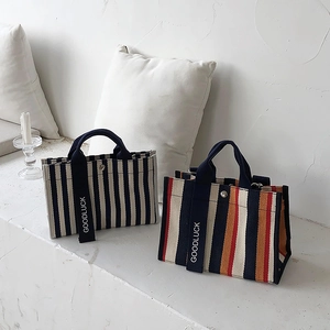 Détail de sacs en toile rayés avec sangles GOODLUCK dans un décor intérieur épuré