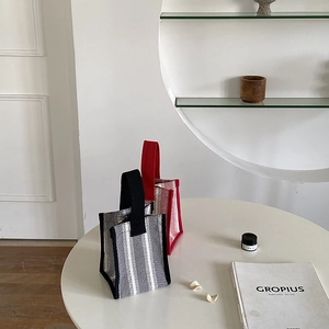 Detailed view of woven striped mini handbags in red and black on a white table