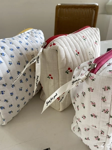 Close-up of quilted floral cosmetic bags with cherry patterns and ribbon zip detail