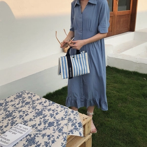 Détail du sac cabas en toile rayé bleu et blanc porté avec une robe d'été midi