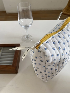 Detail of floral quilted cosmetic bag featuring blue flowers and a yellow zipper closure