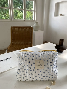 Detail of floral quilted cosmetic bag with alpaca patch and yellow zipper on a sunny ledge