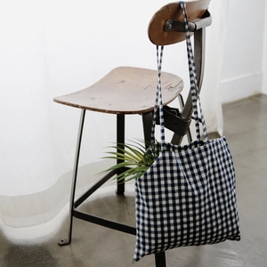 Detail einer dunkelblauen Gingham-Canvas-Tasche mit langen Trägern an einem Stuhl