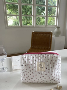Detail of floral quilted cosmetic bag with pink zipper and alpaca patch on white desk