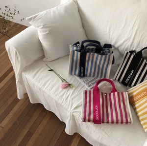 Détail de quatre sacs cabas en toile rayée avec poignées Goodluck posés sur un canapé