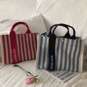 Détail de sacs cabas en toile rayée rouge et bleu avec bandoulière GOODLUCK sur lit