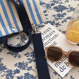 Détail d'un sac cabas en toile rayée bleue avec bandoulière et lunettes de soleil tendance