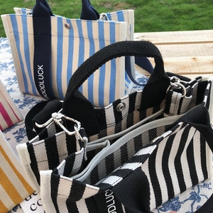 Détail de sacs cabas rayés en toile avec poignées GOODLUCK sur la pelouse