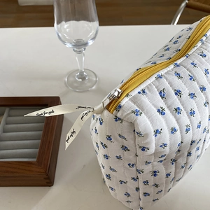 Quilted floral makeup bag with yellow zipper and decorative ribbon on a white desk