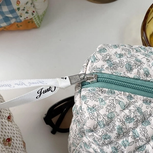 Quilted floral cosmetic bag featuring a metal zipper with a decorative white ribbon handle