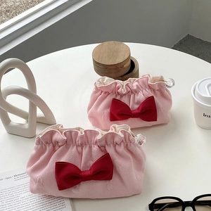 Pink pleated makeup bag set with red satin bows and pearl zipper charms on a desk