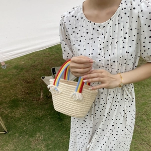 Detalle de un bolso de paja tejido con asa de arcoíris y adornos de flecos blancos