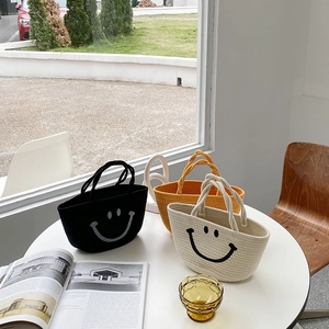 Three straw cotton rope bags with smiley faces in black, yellow, and beige on a table