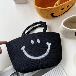 Detail of hand-woven black cotton rope bag with white smiley face and dual handles