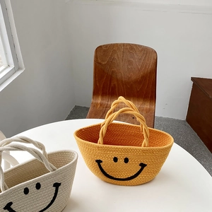 Detail of woven straw handbag featuring a black smiley face and cotton rope handle