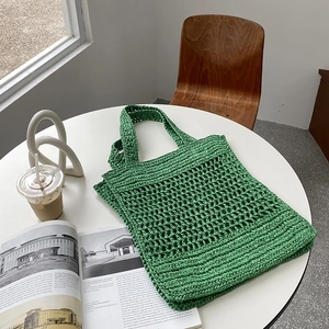 Primer plano del bolso tote tejido verde con textura de paja en una mesa blanca