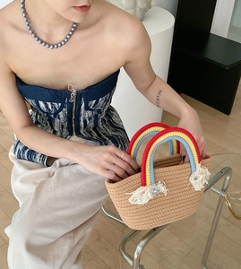 Detalle de bolso de paja trenzada con asa de punto arcoíris y decoración de flecos blancos