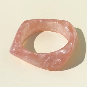 Close-up of pink resin bangle with white marble texture and minimalist geometric design