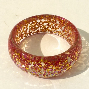 Close-up of wide transparent resin bangle with embedded red and gold glitter flakes
