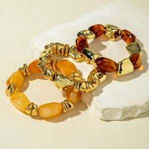 Detail of amber acrylic beads and golden irregular metal charms on elastic bracelets