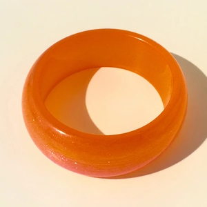 Détail d'un bracelet jonc en résine orange translucide avec paillettes et fini poli