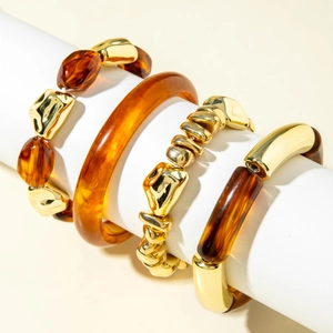 Detailed view of amber acrylic and gold metal beaded bracelet set on white cylinder