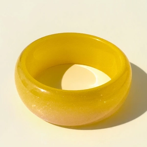 Détail d'un large bracelet en résine jaune avec paillettes dorées et texture translucide