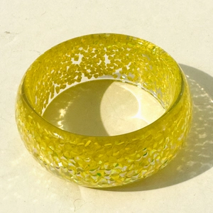 Detail of yellow resin bangle featuring sparkly glitter inclusions and a wide glossy finish