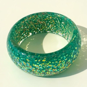 Detail view of wide green resin bangle with embedded colorful laser sequins and sparkles