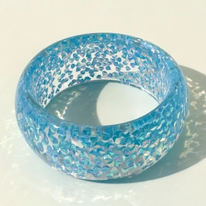 Detail of transparent blue resin bangle with embedded glitter flakes on grey background